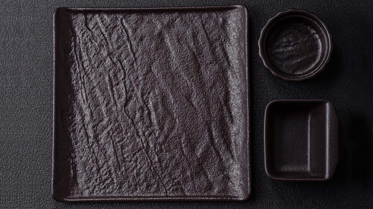 A dark ceramic plate, bowls and chopsticks arranged on a table